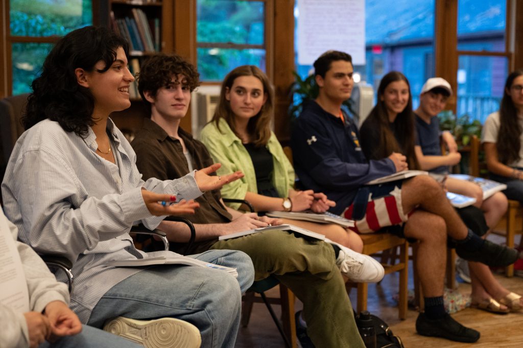 A group of Fellows sit in a room.  One of them is speaking and holds out her hands; the rest look at her. Some are smiling.